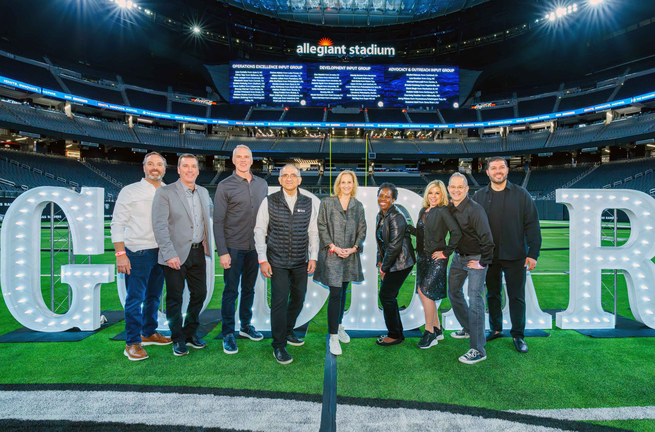Goddard School leadership posed in front of light-up Goddard lettering on the field at Allegiant Stadium