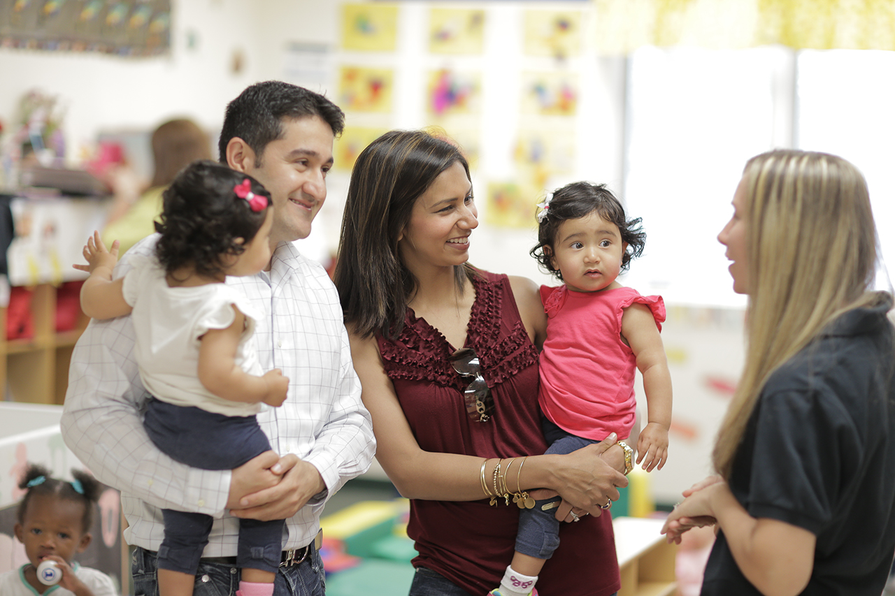 A mother and father smile and talk to a Goddard teacher while holding their twins.