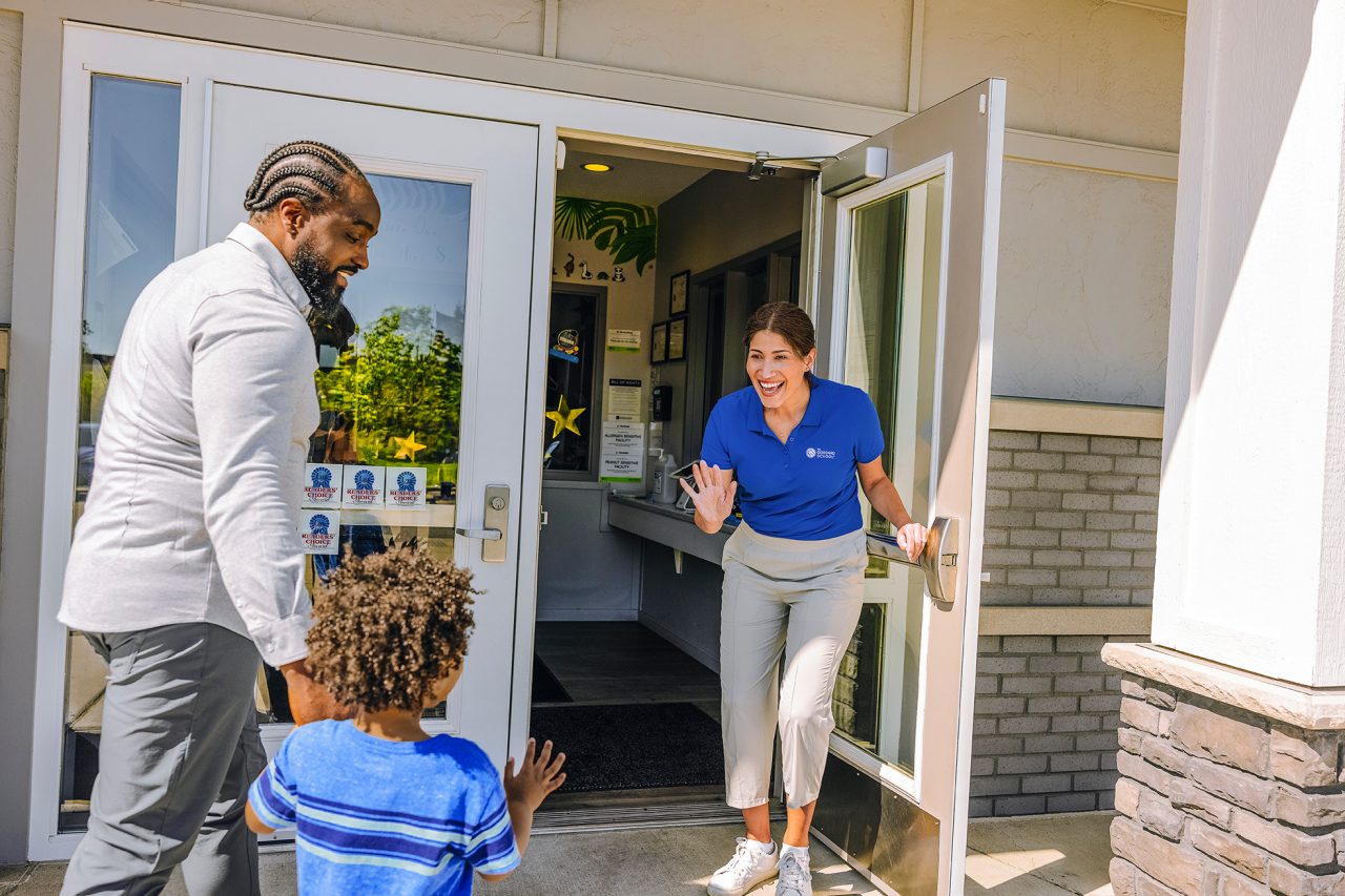 Image of teacher greeting child at entrance of school 